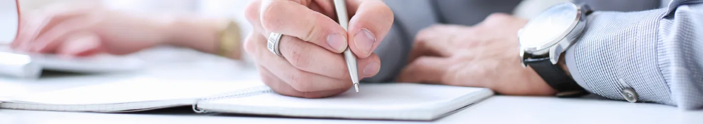 A person wearing a watch and writing in a notebook