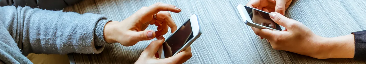 Two people on the opposite sides of a table texting on phones