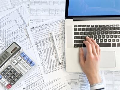 Person doing taxes on a computer on a table covered in tax forms and a calculator